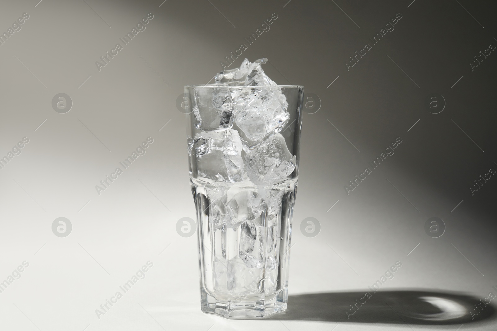 Photo of One glass with ice for refreshing drink on grey background