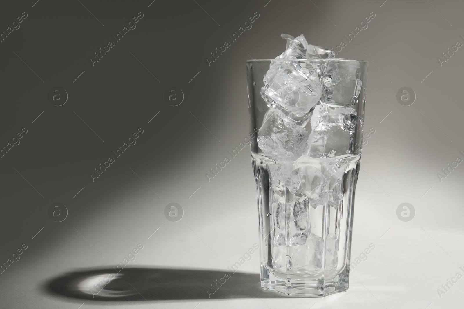 Photo of One glass with ice for refreshing drink on grey background