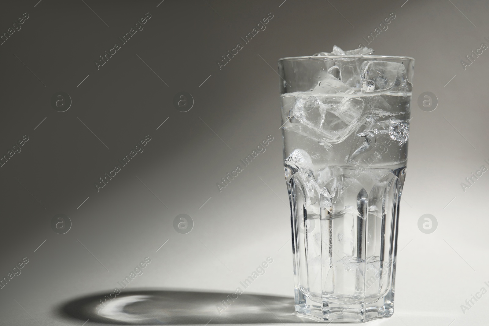 Photo of Refreshing water with ice in glass on grey background. Space for text