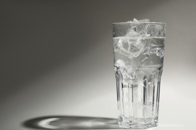 Photo of Refreshing water with ice in glass on grey background. Space for text