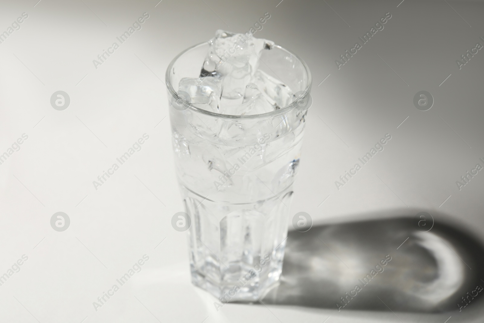 Photo of Refreshing water with ice in glass on grey background, closeup