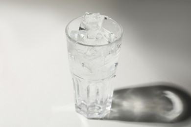 Photo of Refreshing water with ice in glass on grey background, closeup