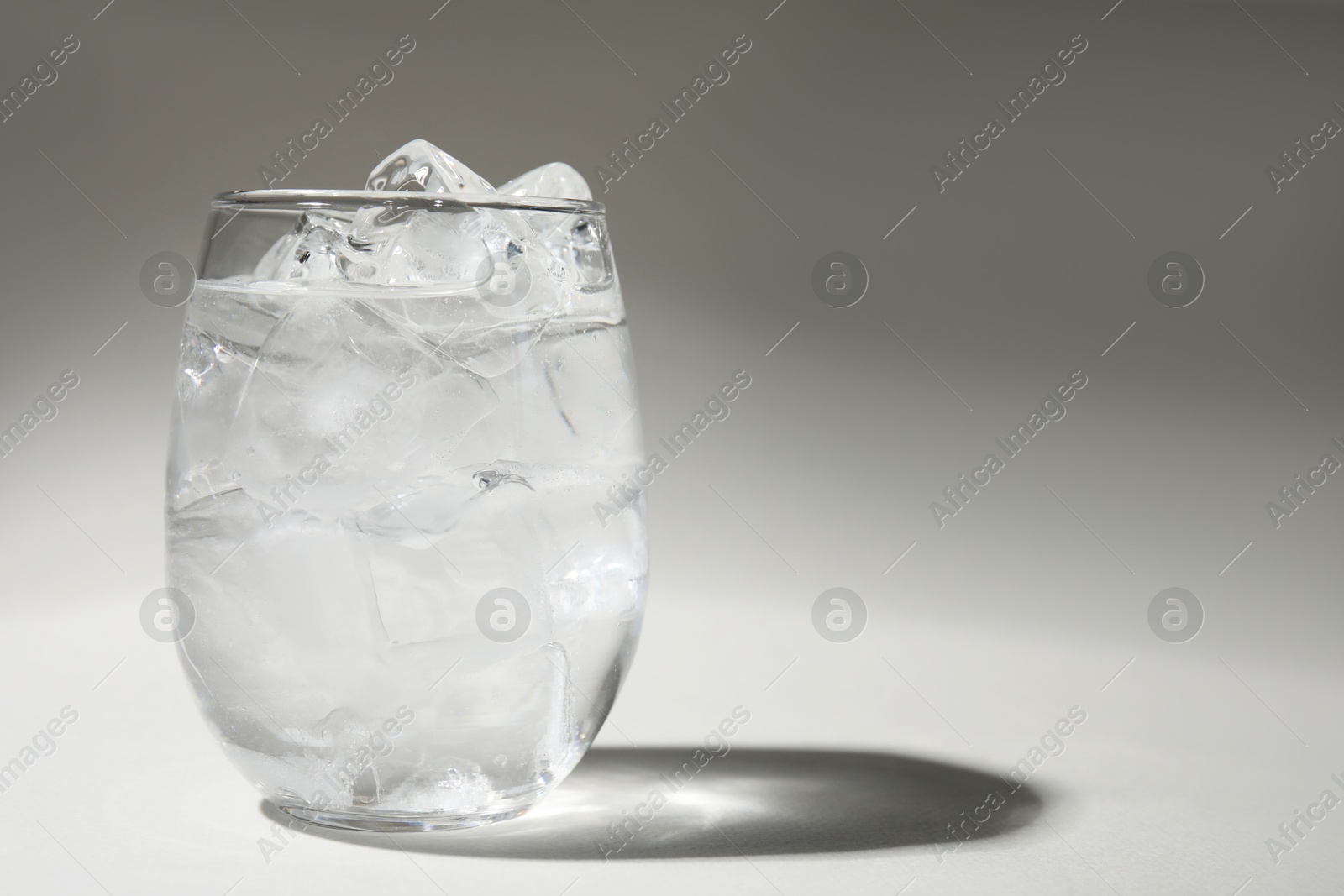 Photo of Refreshing water with ice in glass on grey background. Space for text