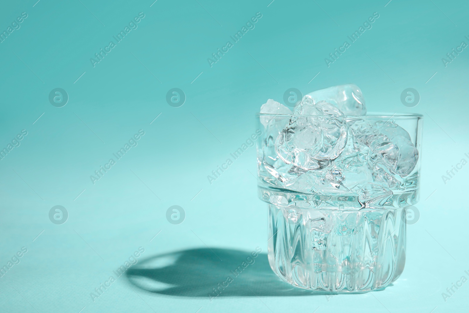 Photo of Refreshing water with ice in glass on turquoise background. Space for text