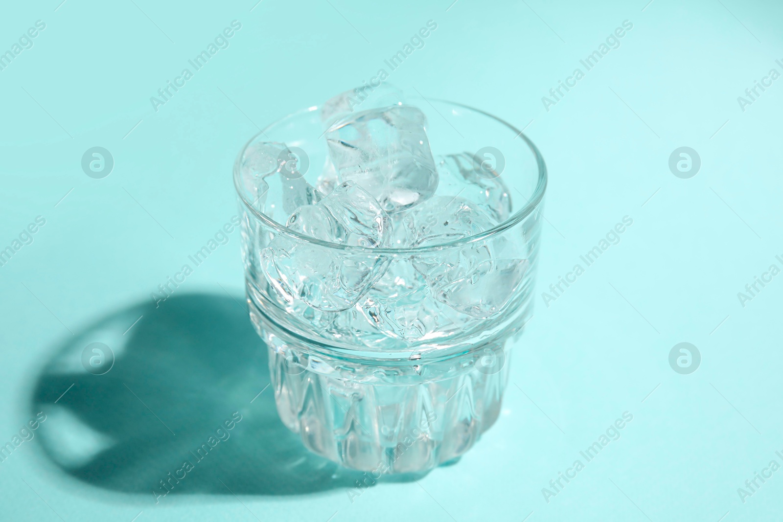 Photo of Refreshing water with ice in glass on turquoise background, closeup