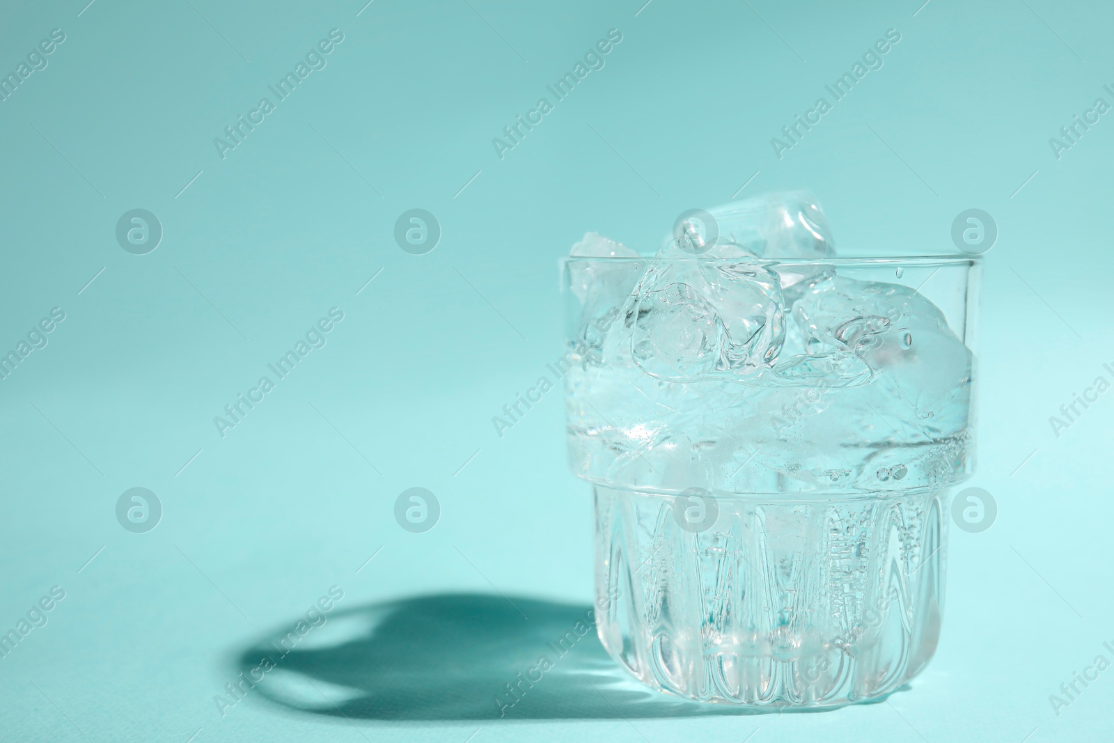 Photo of Refreshing water with ice in glass on turquoise background, closeup. Space for text