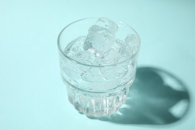 Photo of Refreshing water with ice in glass on turquoise background, closeup