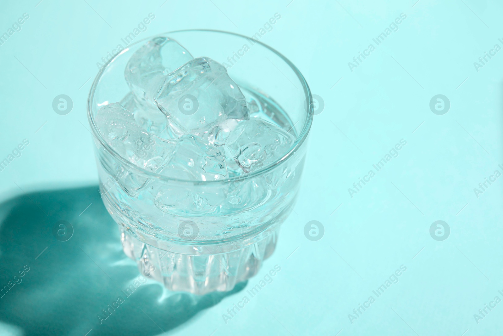 Photo of Refreshing water with ice in glass on turquoise background, closeup. Space for text