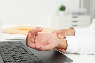 Photo of Carpal tunnel syndrome. Woman suffering from pain in wrist at desk indoors, closeup