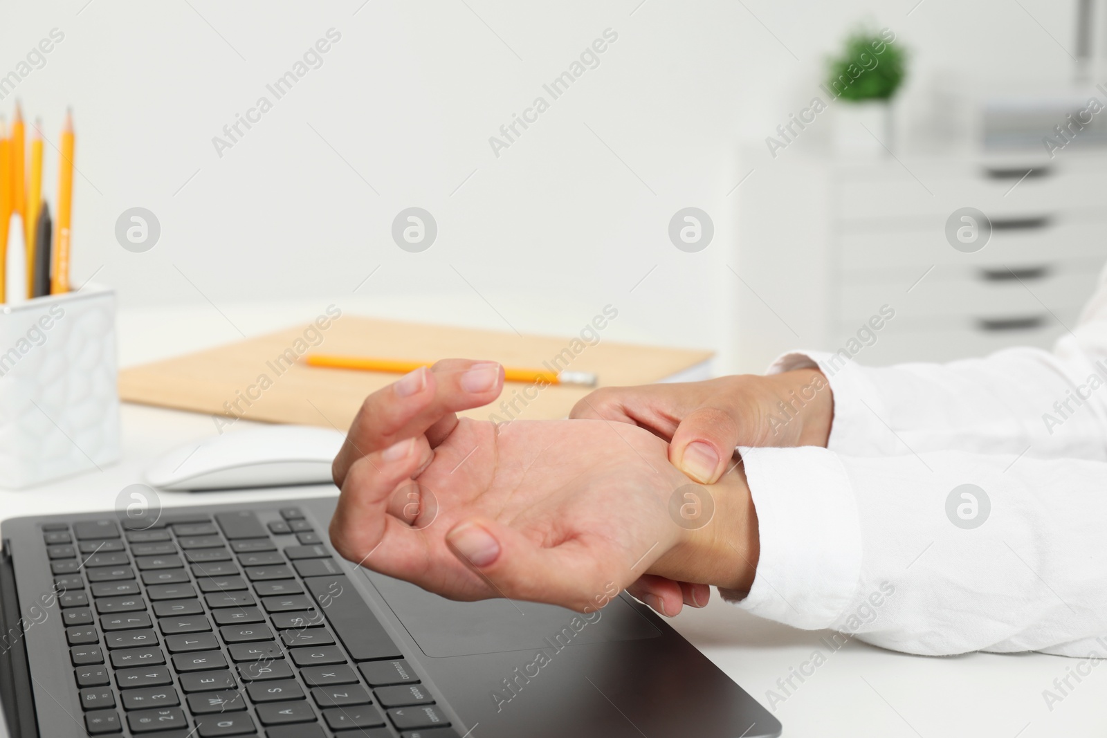 Photo of Carpal tunnel syndrome. Woman suffering from pain in wrist at desk indoors, closeup