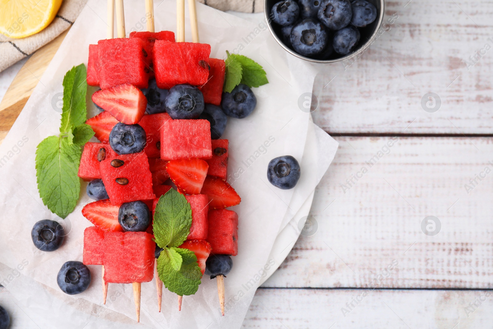 Photo of Skewers with tasty watermelon, strawberries, blueberries and mint on light wooden table, flat lay. Space for text