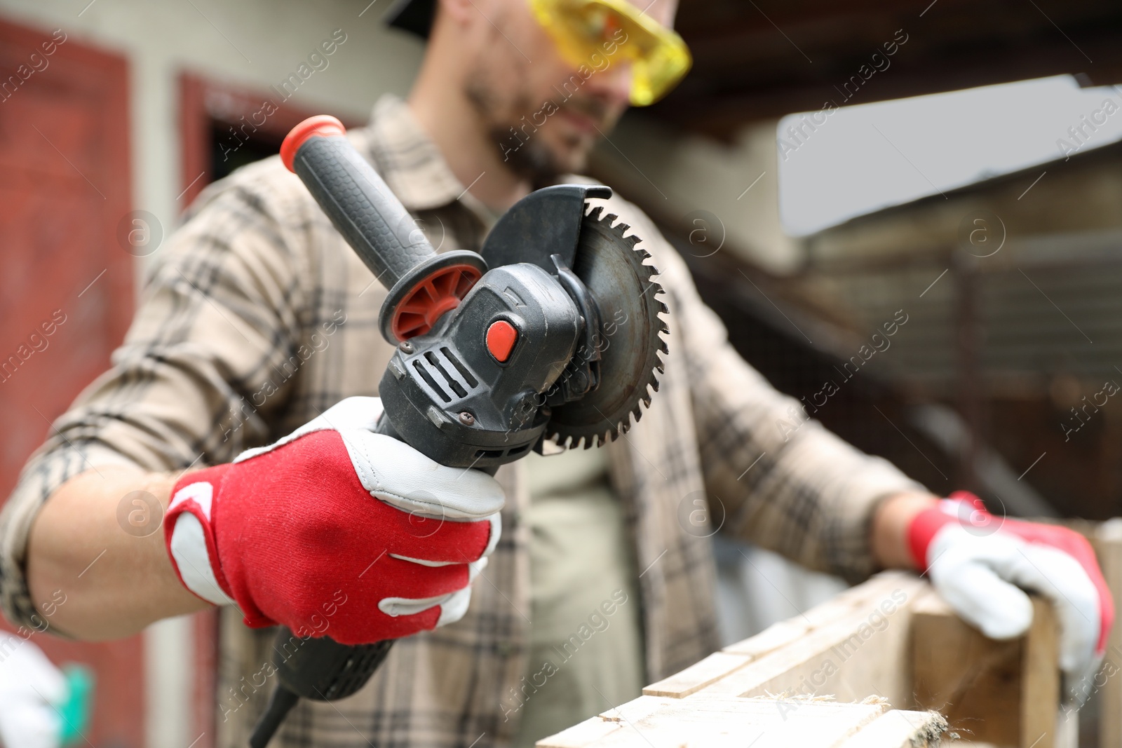 Photo of Man working with angle grinder and wood outdoors, selective focus