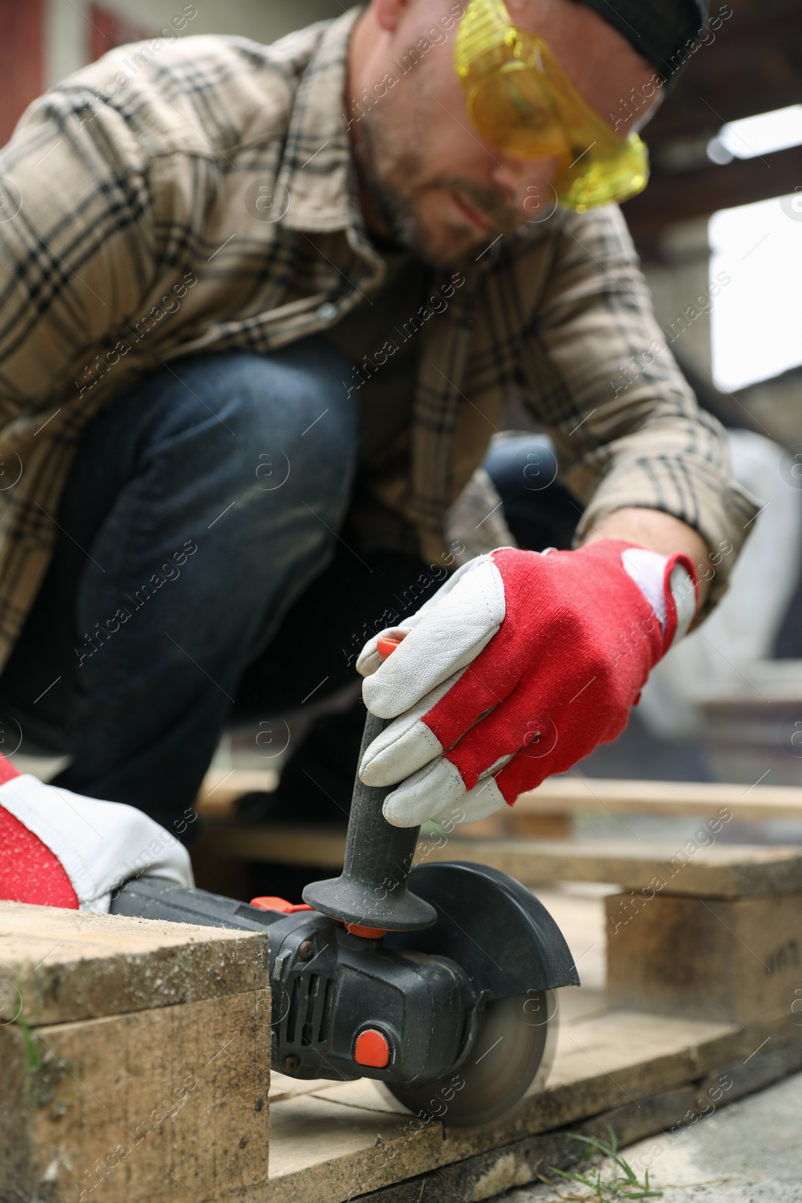 Photo of Man grinding wooden planks with angle grinder outdoors, selective focus