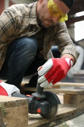 Man grinding wooden planks with angle grinder outdoors, selective focus