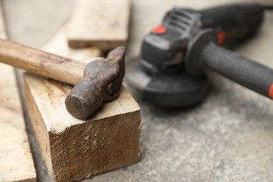 Photo of Hammer, wooden plank and angle grinder on asphalt outdoors, closeup