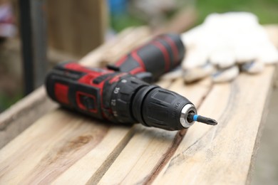 Photo of Electric screwdriver and gloves on wooden table, closeup