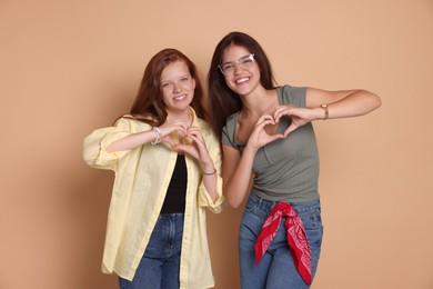 Happy teenage girls making hearts with hands on beige background