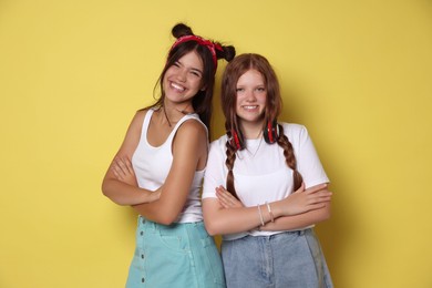 Happy teenage girls with crossed arms on yellow background