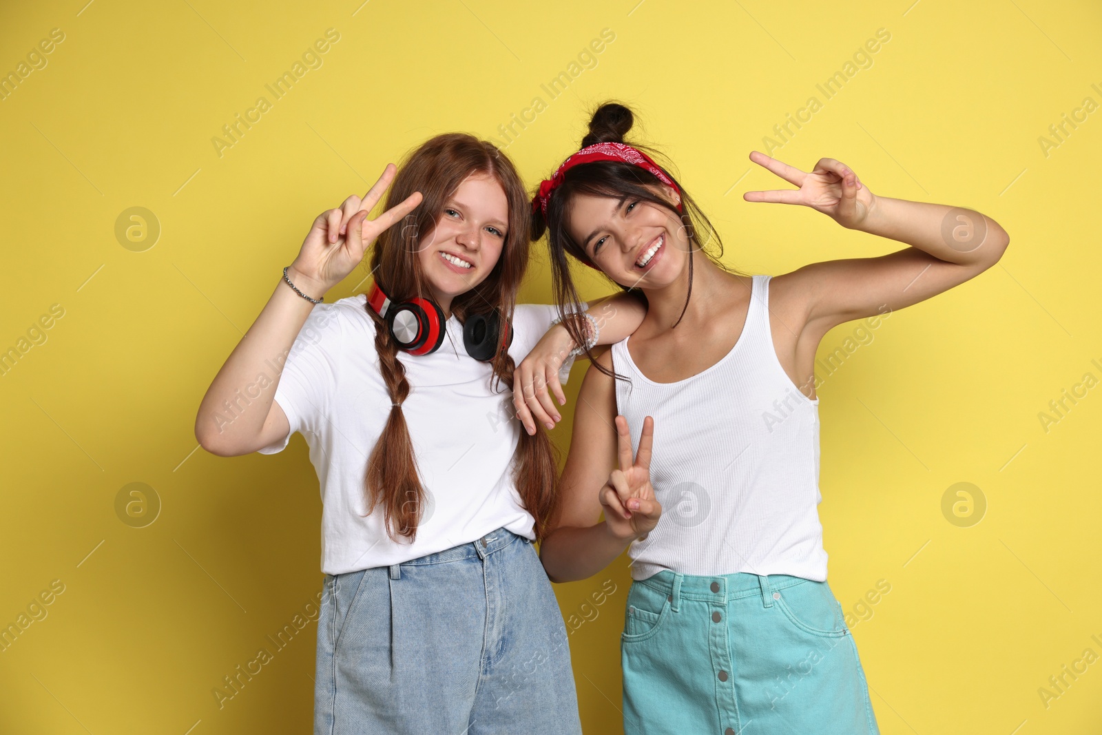 Photo of Happy teenage girls showing peace signs on yellow background