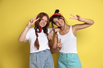 Happy teenage girls showing peace signs on yellow background