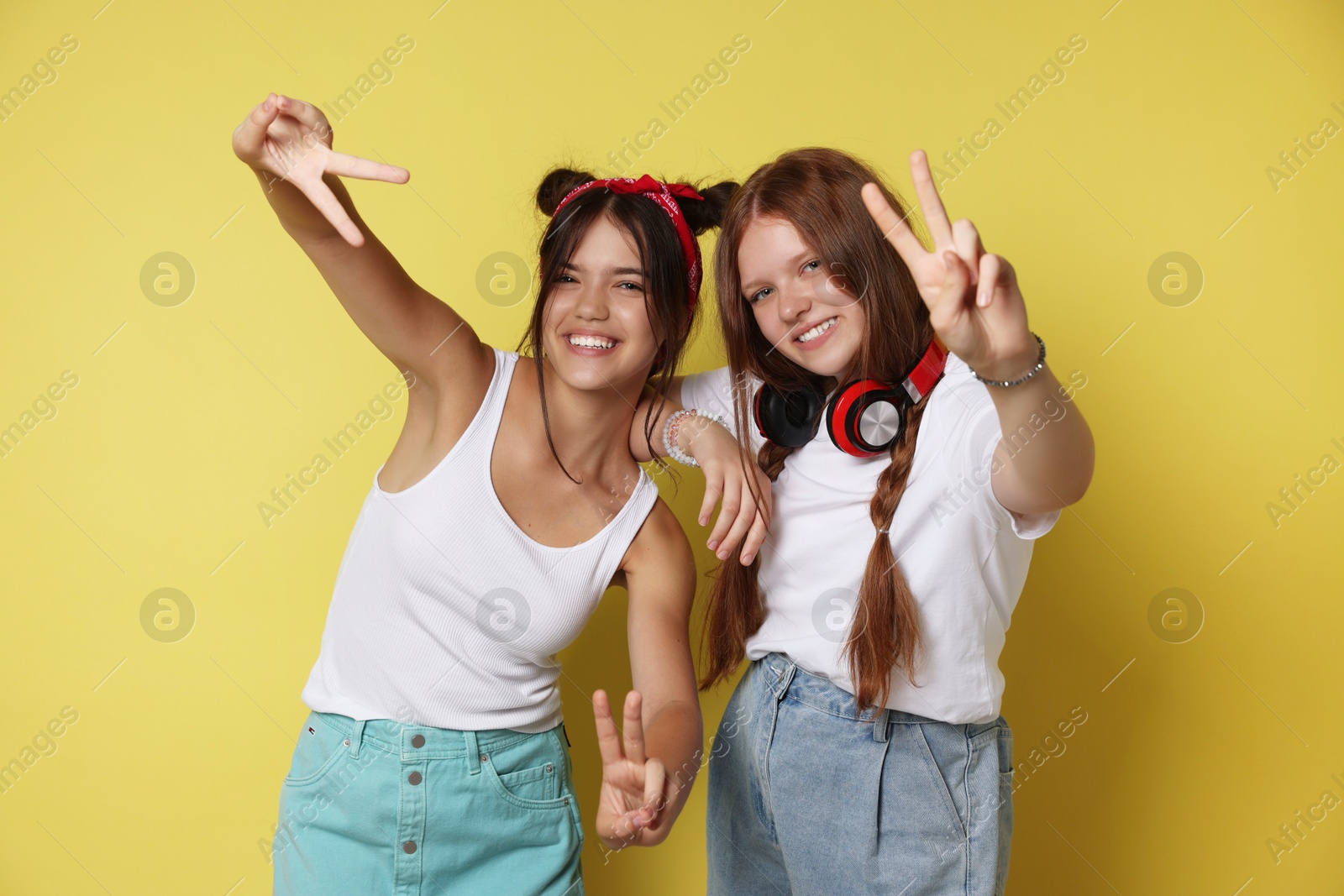 Photo of Happy teenage girls showing peace signs on yellow background