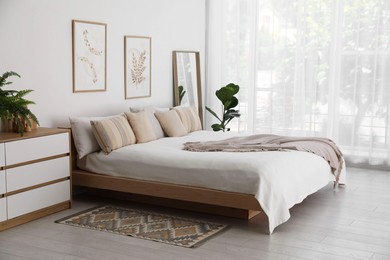 Photo of Large bed, houseplant and full-length mirror near window in room. Stylish bedroom interior