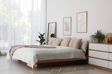 Photo of Large bed, houseplant and full-length mirror near window in room. Stylish bedroom interior