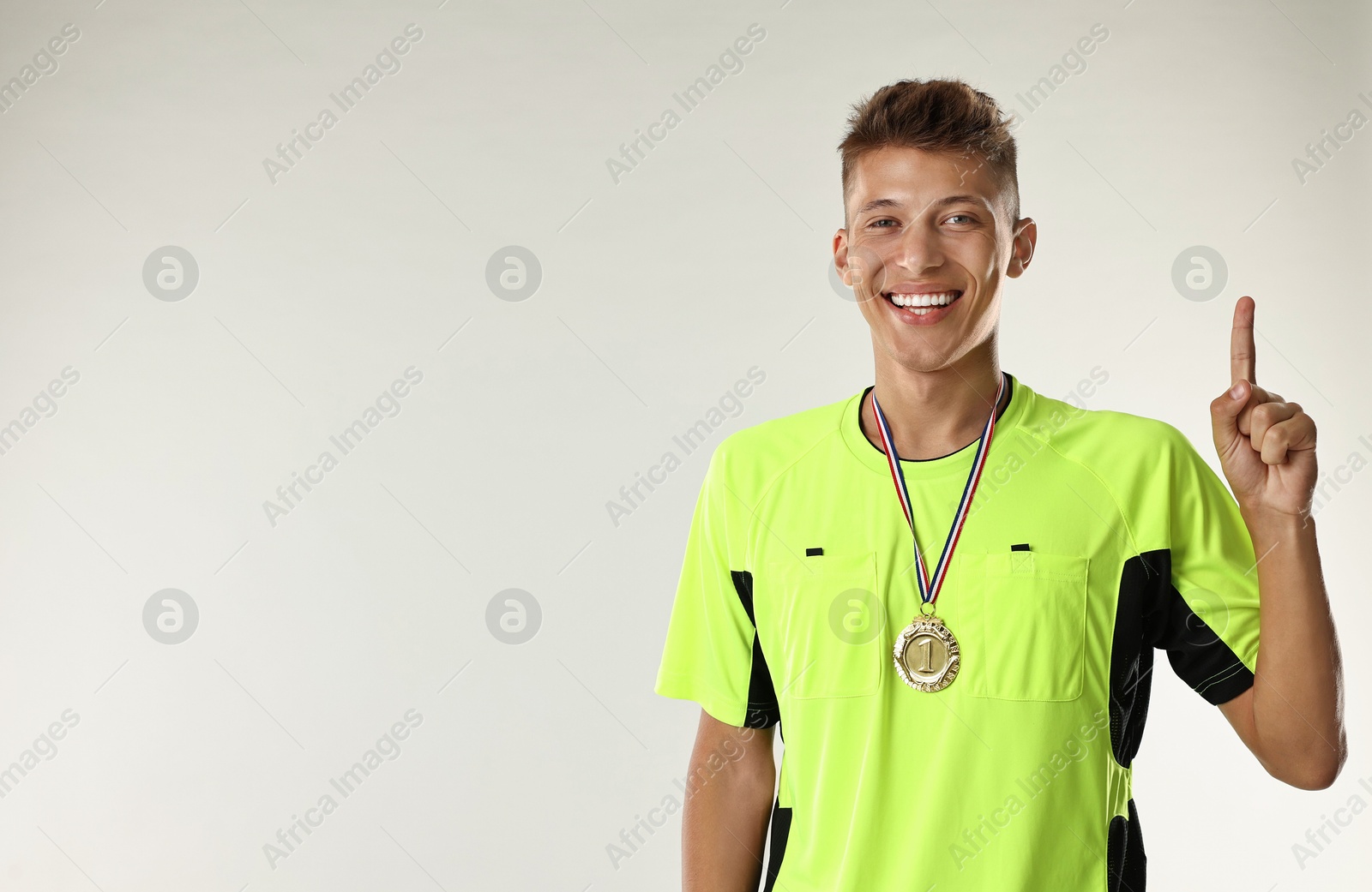 Photo of Happy winner with golden medal pointing upwards on light grey background. Space for text