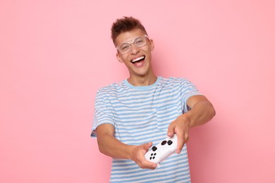 Happy young man playing video games with controller on pink background