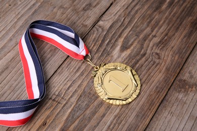 Photo of Golden medal with striped ribbon on wooden background, closeup