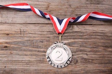 Photo of Silver medal with striped ribbon on wooden background, top view