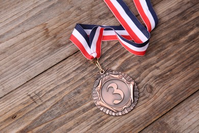 Photo of Bronze medal with striped ribbon on wooden background, top view