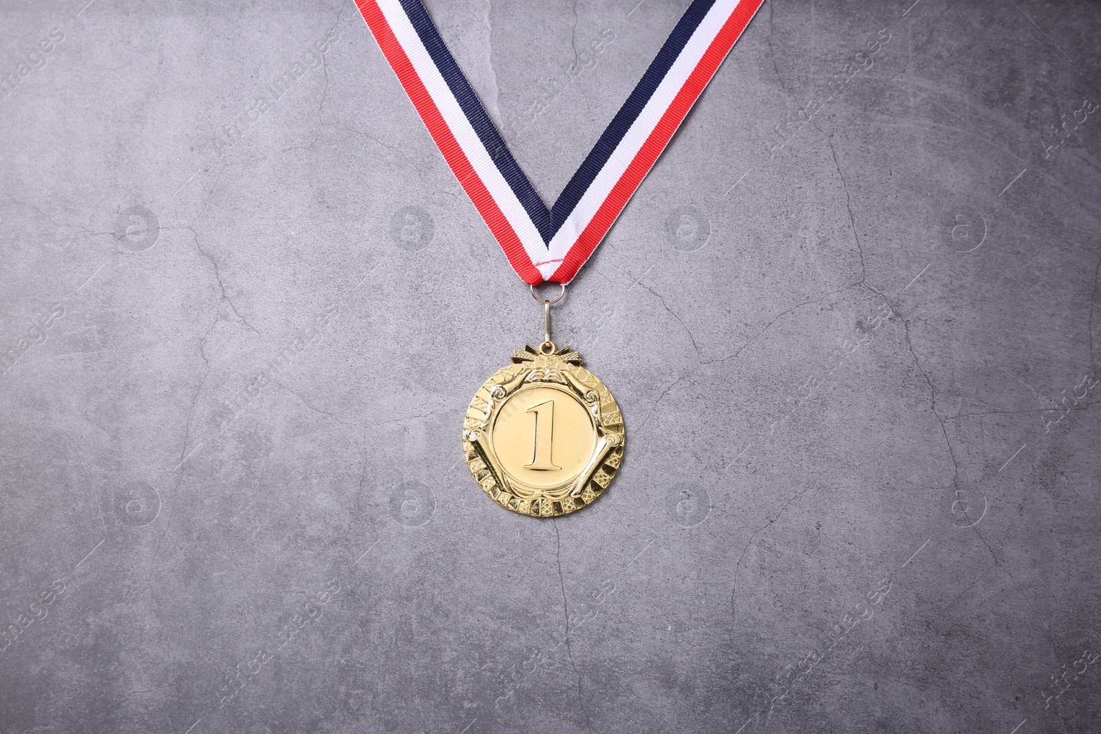 Photo of Golden medal with striped ribbon on grey background, top view