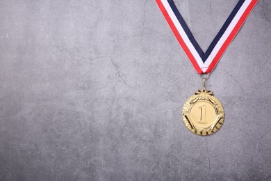 Photo of Golden medal with striped ribbon on grey background, top view. Space for text