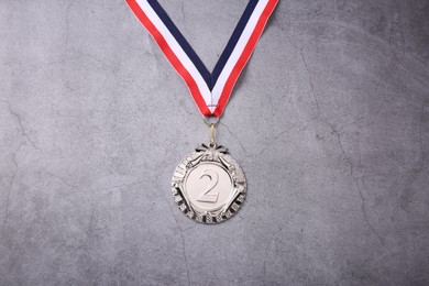 Photo of Silver medal with striped ribbon on grey background, top view