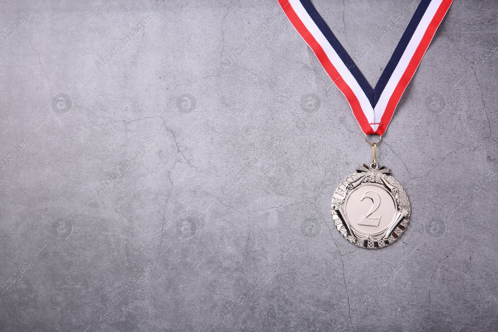 Photo of Silver medal with striped ribbon on grey background, top view. Space for text