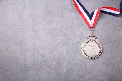 Photo of Silver medal with striped ribbon on grey background, top view. Space for text