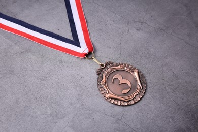 Photo of Bronze medal with striped ribbon on grey background, closeup