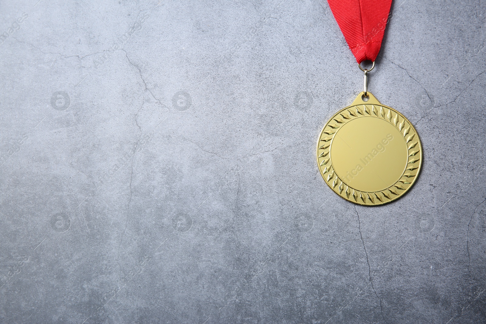 Photo of Golden medal with red ribbon on grey background, top view. Space for text