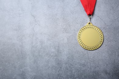 Photo of Golden medal with red ribbon on grey background, top view. Space for text