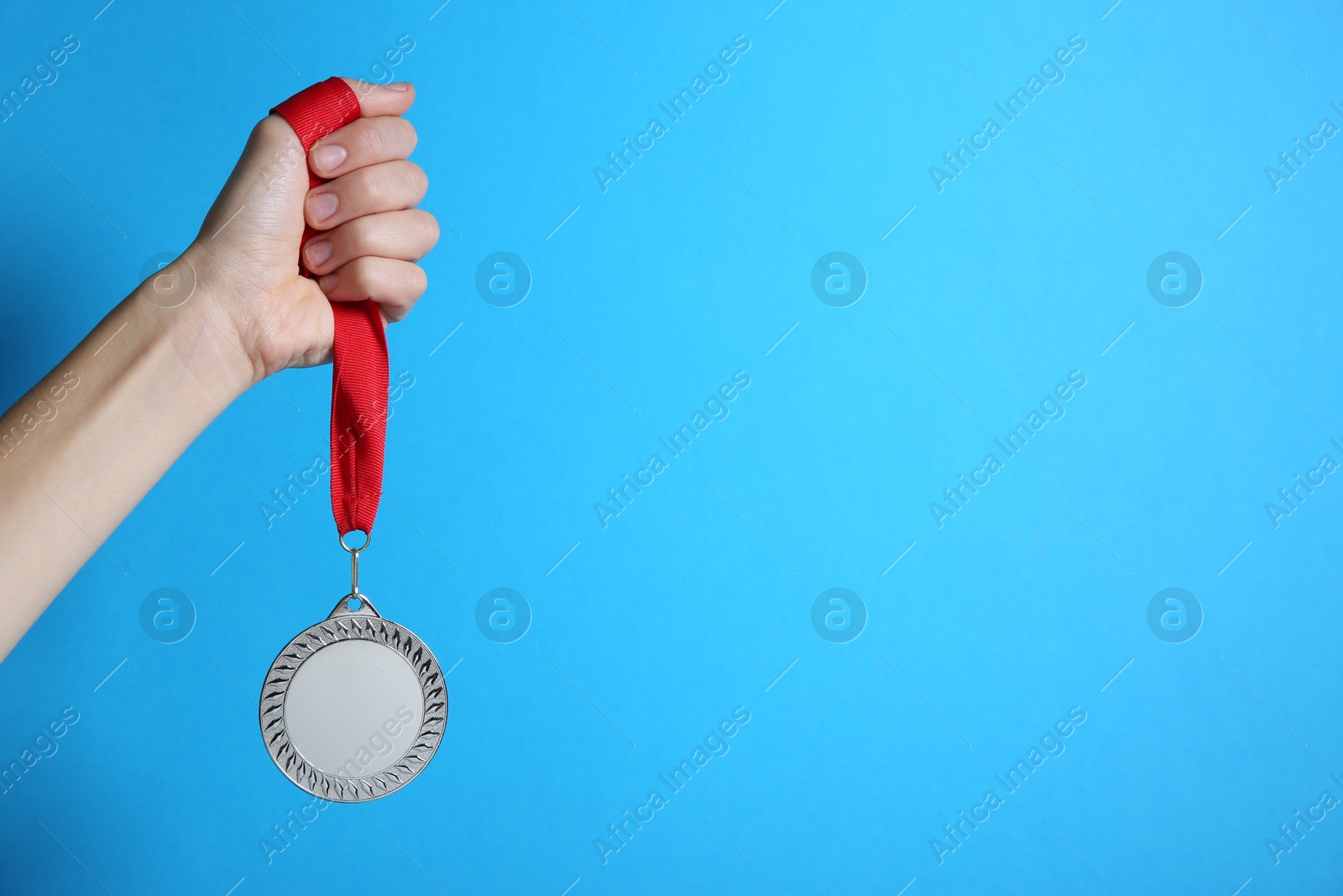 Photo of Woman with silver medal on light blue background, closeup. Space for text