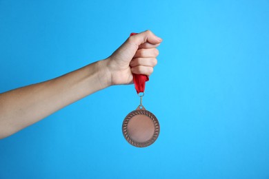 Photo of Woman with bronze medal on light blue background, closeup