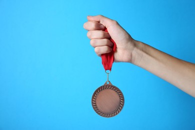 Photo of Woman with bronze medal on light blue background, closeup. Space for text