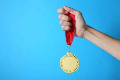 Photo of Woman with golden medal on light blue background, closeup. Space for text