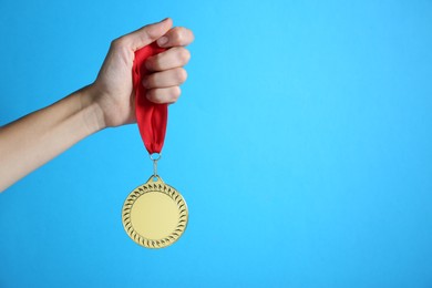 Photo of Woman with golden medal on light blue background, closeup. Space for text