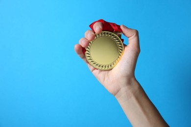 Photo of Woman with golden medal on light blue background, closeup. Space for text