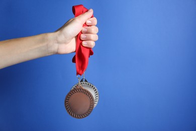 Photo of Woman with bronze and silver medals on blue background, closeup. Space for text