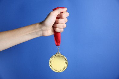 Photo of Woman with golden medal on blue background, closeup