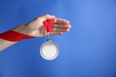 Photo of Woman with silver medal on blue background, closeup. Space for text