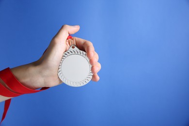 Photo of Woman with silver medal on blue background, closeup. Space for text